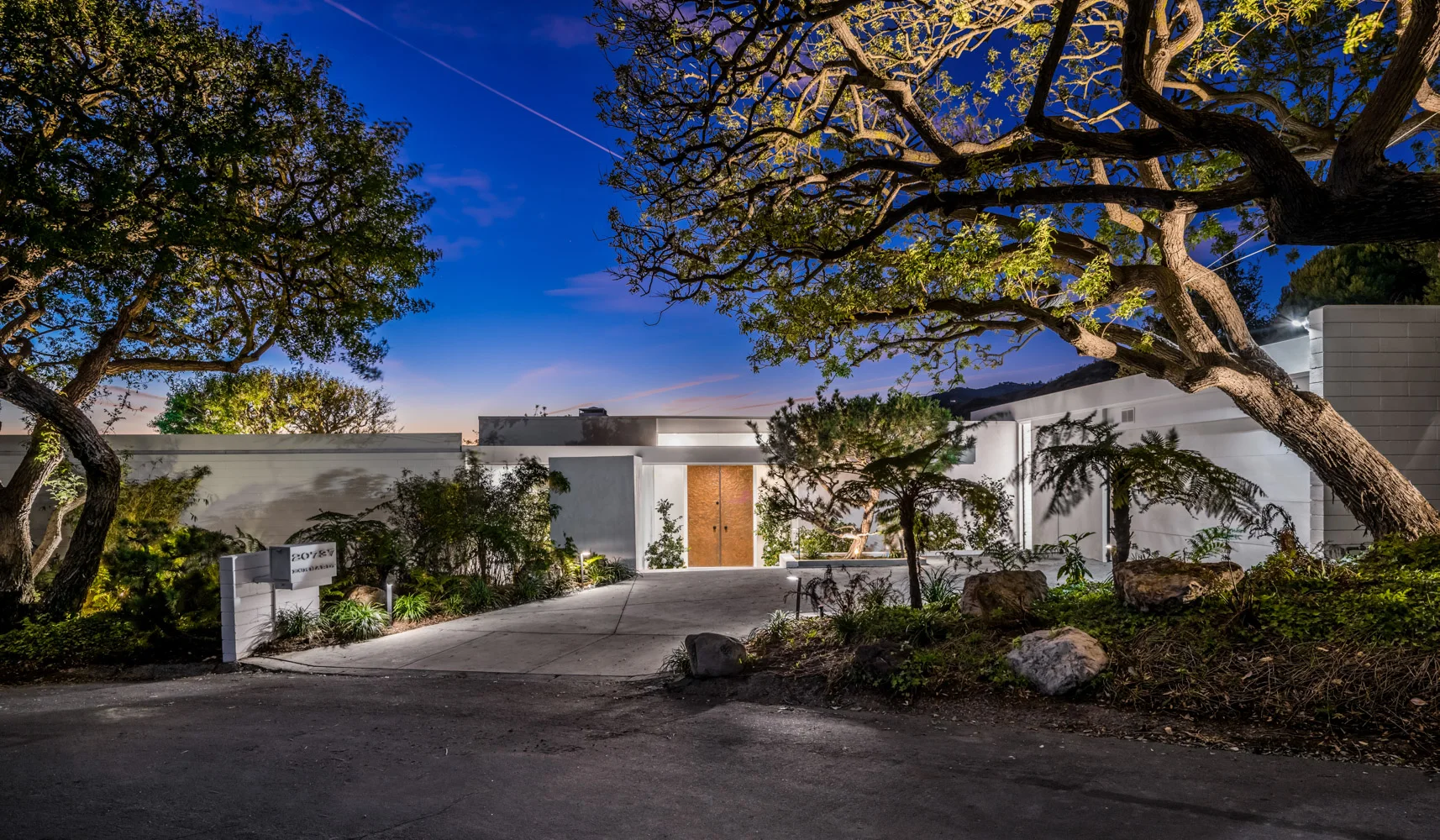 The house at dusk under its oak, lit from within.