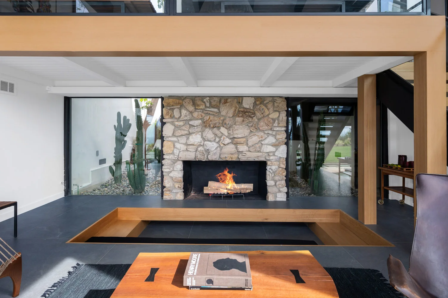 The stone fireplace, lit, under a timber beam.