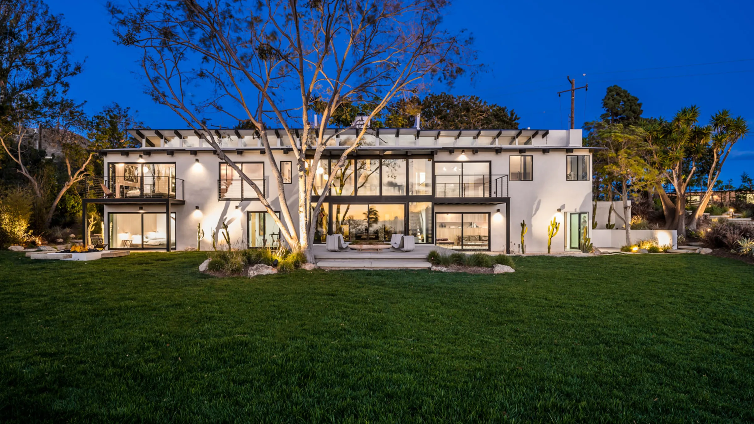 Filaree Heights, Malibu: the house lit from within at dusk, across its lawn.